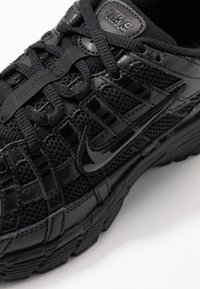 Czarny but sportowy z siateczki i materiałów syntetycznych, z wieloma nakładkami o różnych fakturach oraz błyszczącym logo Nike po bokach.