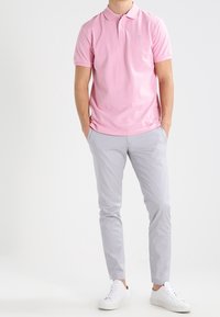 Polo rose clair avec col, associé à un pantalon slim gris clair et des baskets blanches. Tissu lisse et design épuré.