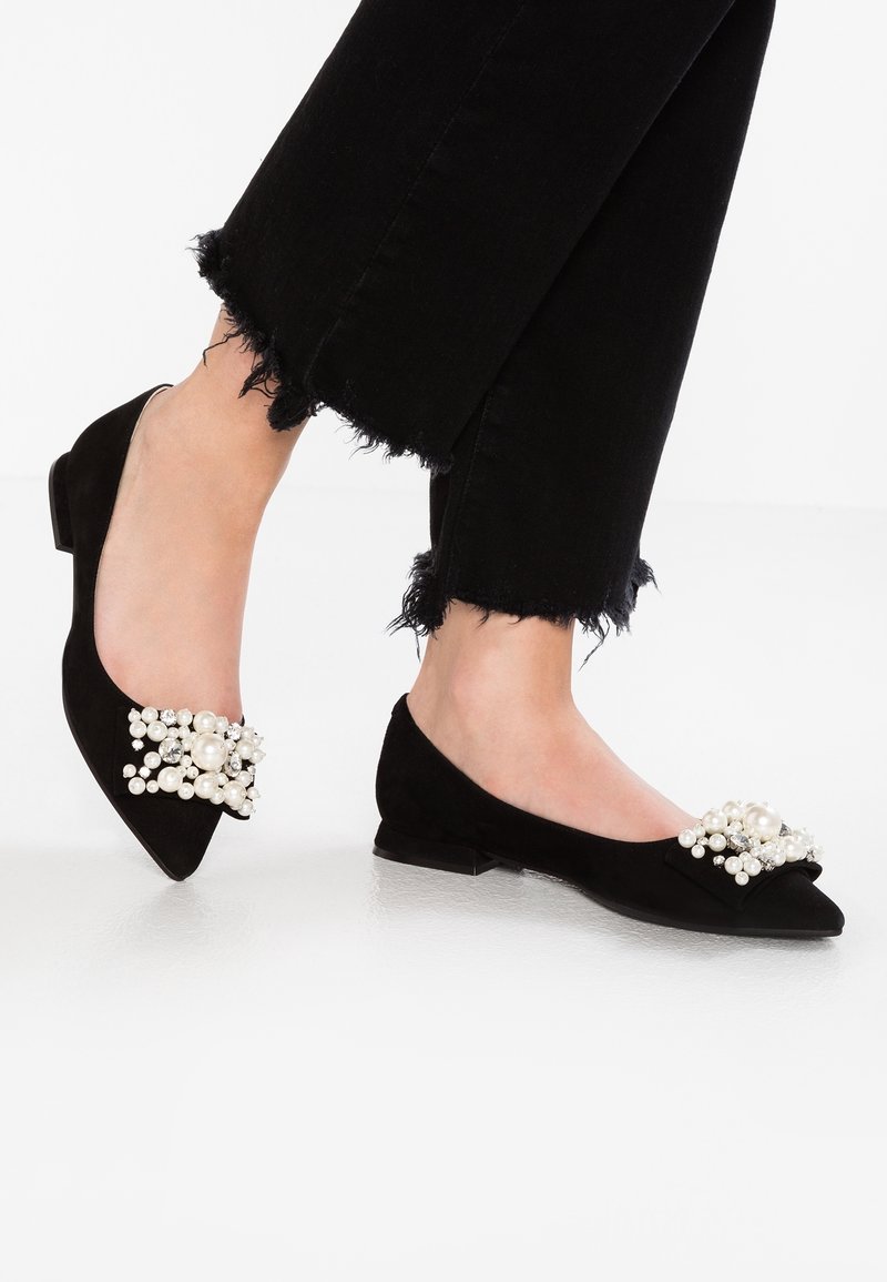 Ballerines noires à bout pointu ornées de perles et de strass, portées avec un pantalon noir à ourlet effiloché.