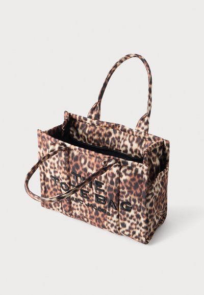 Sac cabas imprimé léopard avec deux poignées et texte noir "The Tote Bag Marc Jacobs" sur le devant, ouverture supérieure montrant la doublure intérieure noire.