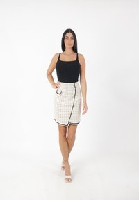 Débardeur noir avec bretelles réglables, associé à une jupe portefeuille blanche à carreaux avec bord noir et un petit détail de poche.
