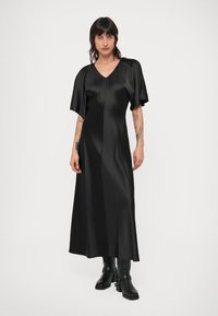 Čierne saténové šaty s výstrihom do V a krátkymi, širokými rukávmi; majú hladkú textúru a splývavú siluetu dosahujúcu až po členky.