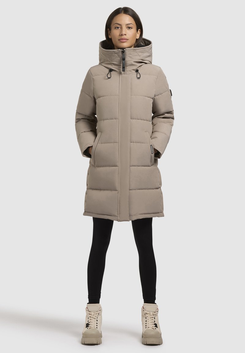 Cernă pură de iarnă, bej, cu guler înalt, închidere cu fermoar și șnururi ajustabile. Mâneci lungi și buzunare laterale completează designul.