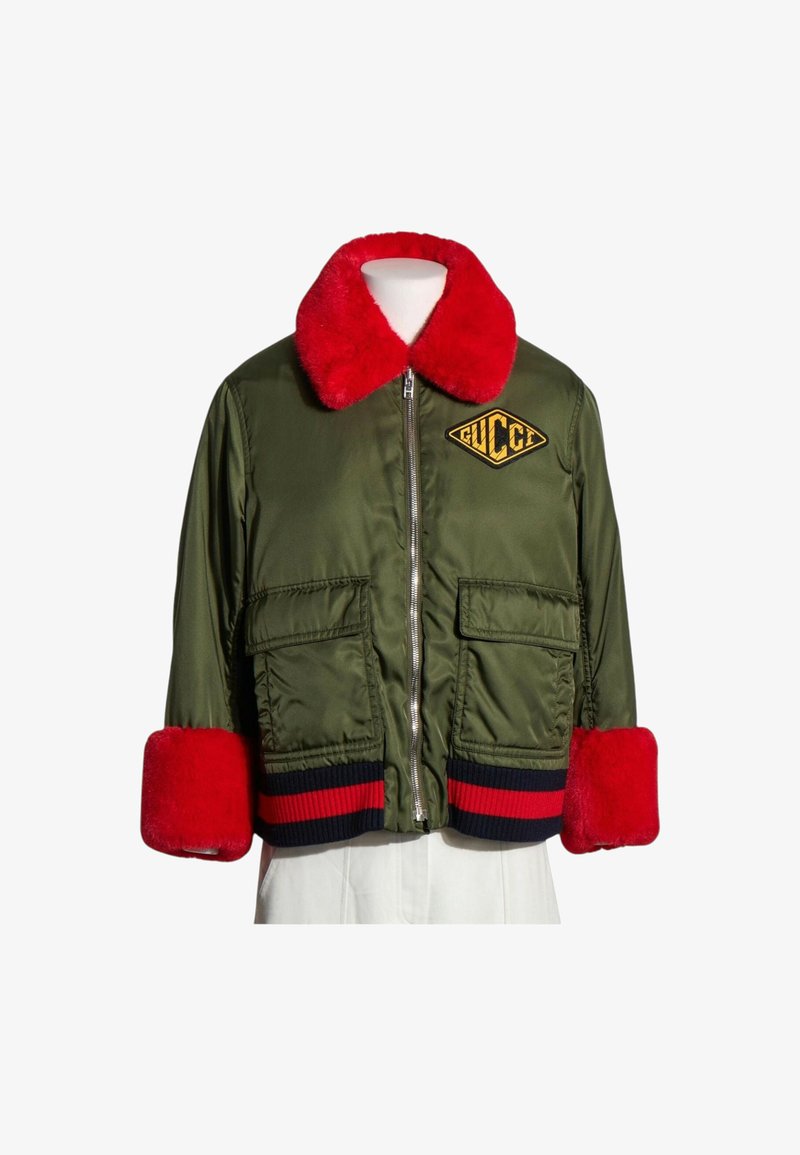 Veste bomber verte avec col en fourrure rouge vif et poignets, fermeture éclair à l'avant, deux poches avant et écusson avec logo Gucci sur la poitrine