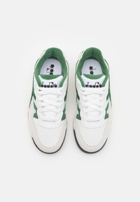 White sneakers with green suede accents, perforated texture, and white laces. Features a branded insole and a rubber outsole.
