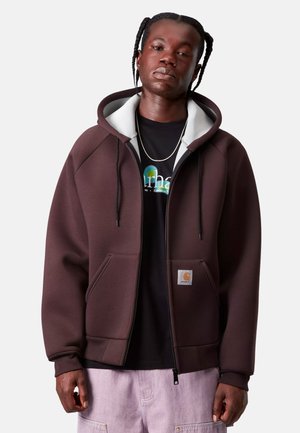 Felpa con zip marrone, con interno grigio, grandi tasche frontali, cordini neri e una patch con logo sulla tasca inferiore.