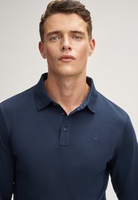 Polo shirt a maniche lunghe di colore navy, caratterizzato da una texture morbida, un colletto e tre bottoni sul davanti, con un logo ricamato sul petto.