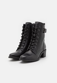 Bottes chevilles en cuir noir avec un bout arrondi, un laçage à l'avant et une boucle décorative sur le côté. Elles possèdent un talon empilé.