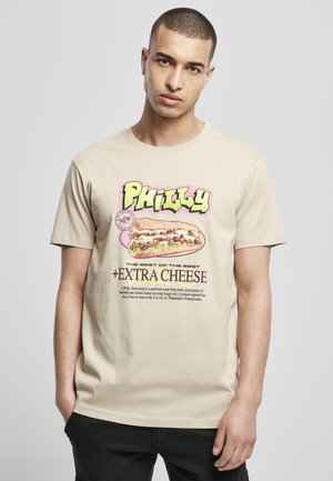 Beige bomulls t-skjorte med en fargerik illustrasjon av en Philly cheesesteak med fet tekst og grafiske aksenter. Korte ermer, rund hals.