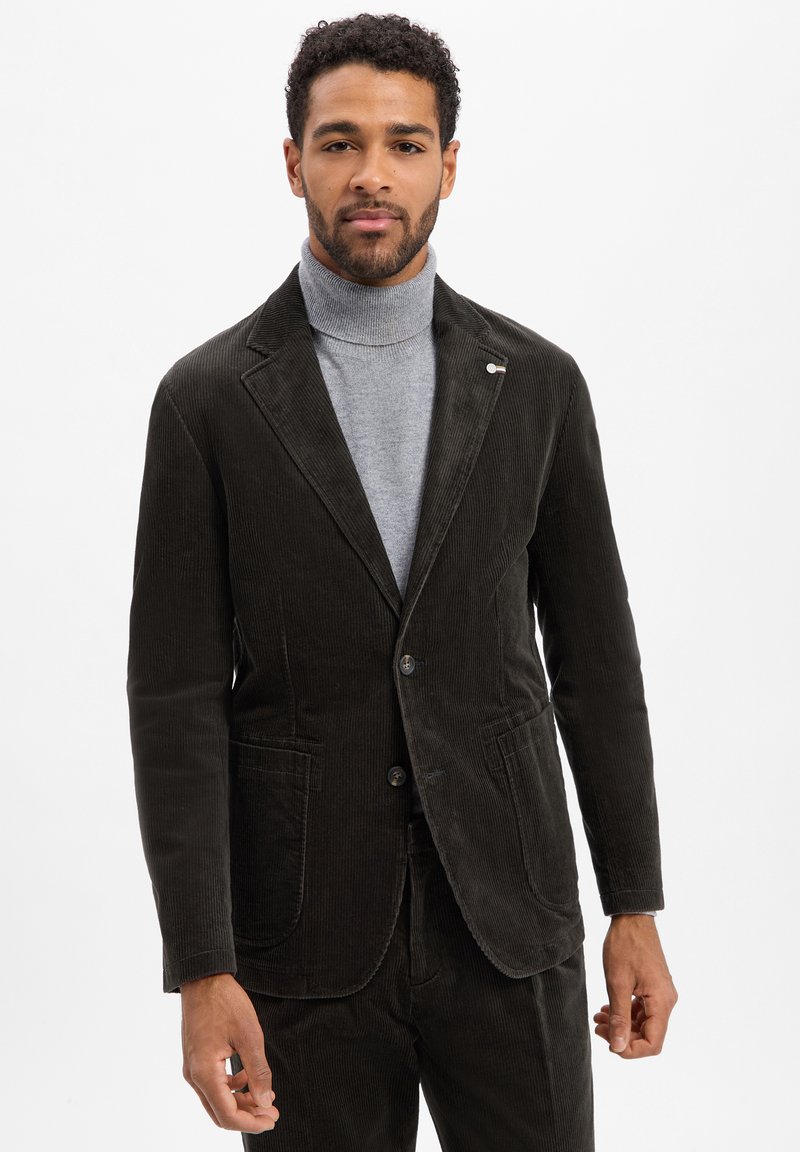 Dunkelbrauner Cordblazer mit schmalem Revers, zwei Knöpfen und Fronttaschen. Über einem grauen Rollkragenpullover getragen. Glatte Textur.