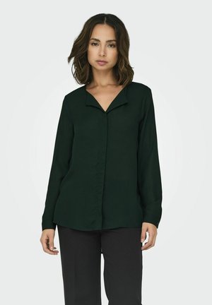 Donkergroene blouse met lange mouwen, heeft een v-hals en een zachte textuur. Kenmerkt zich door een knoopsluiting aan de voorkant en een lichte draping aan de zoom.