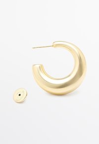 Guld hoops örhängen med en böjd design, som har en glänsande slät yta och en tunn stift. Inkluderar en liten cirkulär baksida.