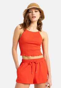 Röd ribbad crop top med scalloped nederkant som matchas med röda shorts med dragsko. Modellen bär också en stråhatt.