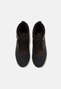 Scarpe da trekking marroni e nere con colletto imbottito, pelle texture e lacci a motivi su una suola texturizzata. Progettate per l'uso all'aperto.