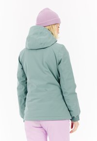 Světle zelená nepromokavá bunda s kapucí, elastickými manžetami a volným střihem. Na sobě má světle fialový kulich. Hladká textura.