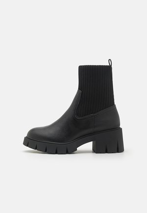 Mustad mustasaapad ribakudumisega ülemise osa, sileda nahast keha, plokknukk ja tugeva kummitald. Lihtne, kaasaegne disain.