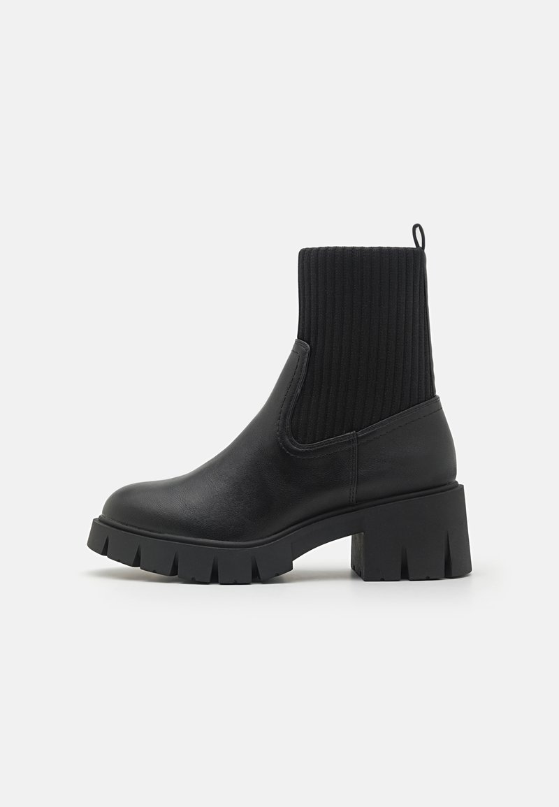 Black ankle boot with a ribbed knit upper, smooth leather body, block heel, and chunky rubber outsole. Simple, modern design.