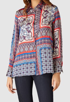 Blusa a maniche lunghe con una stampa geometrica multicolore in blu, rosso e crema. Tessuto leggero e morbido; chiusura con bottoni sul davanti e colletto.