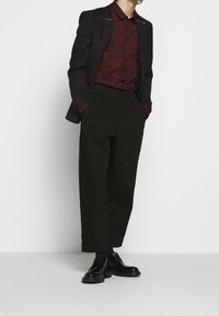 Blazer nero con hardware argentato, camicia bordeaux texturizzata, pantaloni neri a vita alta e scarpe nere con lacci, styling casual.