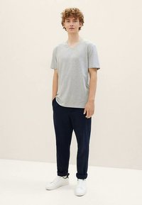 T-shirt grigia con scollo a V, taglio morbido, abbinata a pantaloni jogger blu navy e scarpe da ginnastica bianche. Texture liscia, design casual, senza motivi o accenti visibili.