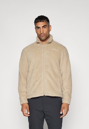 Beige, zip-up fleece jacket with a high collar and textured surface, featuring two front pockets and a logo on the upper left chest.