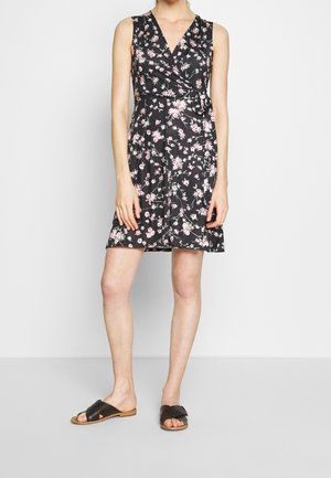 Mouwloze zwarte jurk tot op de knie met roze bloemenprint en een wikkel taille, gedragen met zwarte platte sandalen met open tenen door een model.