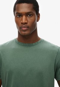 T-shirt en coton à col rond de couleur vert discret. Manches courtes, coupe légèrement décontractée, texture lisse, sans motifs ni accents prononcés.