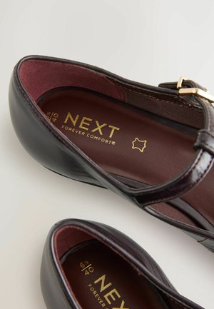 Burgundy läderballerinaskor med en spännestrap. Insidan har guldbröm och en brun innersula, med kontrasterande burgundy-fodring och en slät yta.