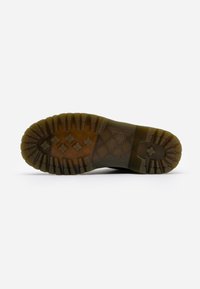 Semelle de botte en caoutchouc marron avec des crampons profonds et un motif de croix et de rectangles pour une meilleure traction, sur un fond blanc.