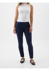 Pantalons bleu marine ajustés avec une texture lisse, présentant un design à plat, des passants de ceinture et des poches, associés à un haut sans manches blanc.