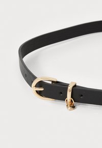 Cinturón de cuero negro con hebilla circular en tono dorado y un pequeño colgante en forma de corazón, textura suave y con múltiples agujeros de ajuste.