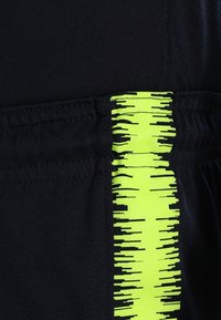 Gros plan d'un tissu noir avec une bande verticale jaune néon comportant des lignes horizontales noires irrégulières.