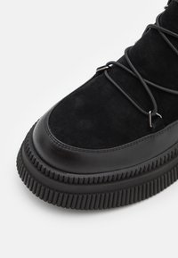 Zwarte suède en leren schoen met een dikke geribbelde zool, met een ronde neus en vetersluiting met metalen hardware accenten.