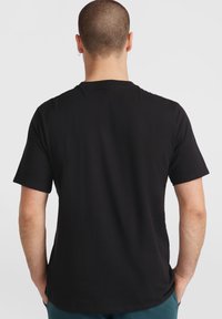 Camiseta negra de manga corta hecha de algodón, con cuello redondo clásico y una textura suave, vista desde la parte posterior.