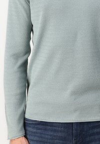 Lichtblauw, geweven shirt met lange mouwen en een geribbelde patroon, voorzien van een ronde halslijn en aansluitende mouwen. Gepaarde met donkere spijkerbroek.