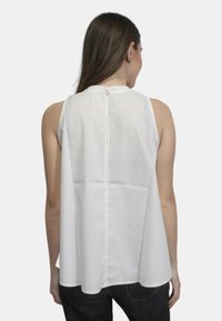 Top bianco senza maniche con scollatura arricciata, tessuto testurizzato e chiusura a occhiello sul retro. Vestibilità ampia con orlo dritto.