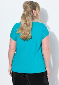 Lyhythihainen turkoosi paita, jossa on pyöreä kaula-aukko ja sileä pinta, yhdistettynä mustiin, ribattuihin housuihin.