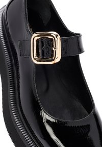 Zapato Mary Jane de charol negro con punta redondeada, detalle de hebilla dorada y suela texturizada. Acabado suave y tacón ligeramente elevado.
