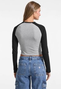 Long-sleeve crop top with a gray body and black raglan sleeves, paired with high-waisted blue denim cargo pants featuring back pockets.