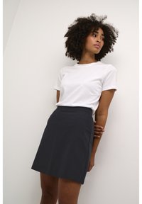 T-shirt en coton blanc associé à une jupe A-line navy foncé. La jupe présente une texture lisse et un design simple.