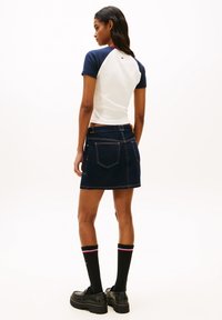 Λευκό τοπ με κοντά μανίκια και μπλε ναυτικό raglan μανίκια, σε συνδυασμό με σκούρα τζιν φούστα. Φοράει μαύρες κάλτσες με κόκκινες και λευκές ρίγες και παπούτσια με πλατφόρμα.