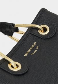 Černá texturovaná kožená taška s rohy, se zlatými kovovými rukojeťmi a logo Emporio Armani Milano 1981 embosované zlatými písmeny.