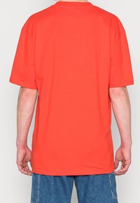 Červené bavlněné tričko s volným střihem, krátkými rukávy a kulatým výstřihem. Bezšvový zadní díl, bez vzorů a potisků. Kombinováno s džínovými šortkami.