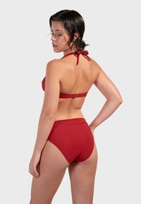 Červený bikiny set s halter topom a viazaním na krku, a s vysokým pásom. Hladká tkanina, minimalistický dizajn a metalické akcenty.