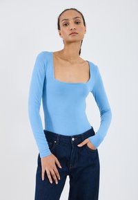 Lys blå langermet bodysuit med firkantet halslinje, kombinert med mørkeblå denimjeans. Glatt tekstur, tettsittende design, minimal detaljering.