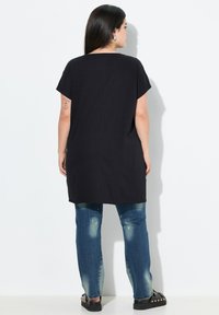 Zwarte tuniek met een losse pasvorm en korte mouwen, gecombineerd met versleten blauwe jeans met lichte beschadigingen en zwarte platte schoenen.