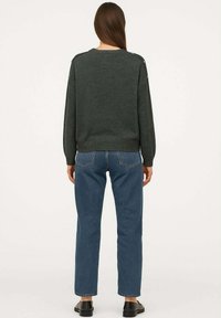 Maglione a maglia verde scuro con colletto rotondo, impreziosito da bottoni sugli spallacci. Abbinato a jeans blu a gamba dritta e scarpe nere.