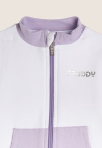 Prenda blanca con cremallera y cuello y bolsillo color lila. Presenta letras metálicas "FREDDY" en el pecho. Textura de tela lisa.