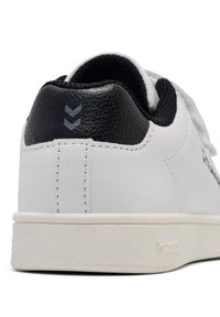 Vita sneakers med ovandel i texturerat läder, svart hälackent, grå logodetaljer och en slät gummisula. Snörningsdesign synlig.
