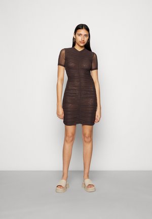 Vestido curto castanho com um design texturizado e franzido, e mangas curtas e transparentes. Modelo usa sandálias de plataforma bege, de pé contra um fundo neutro.